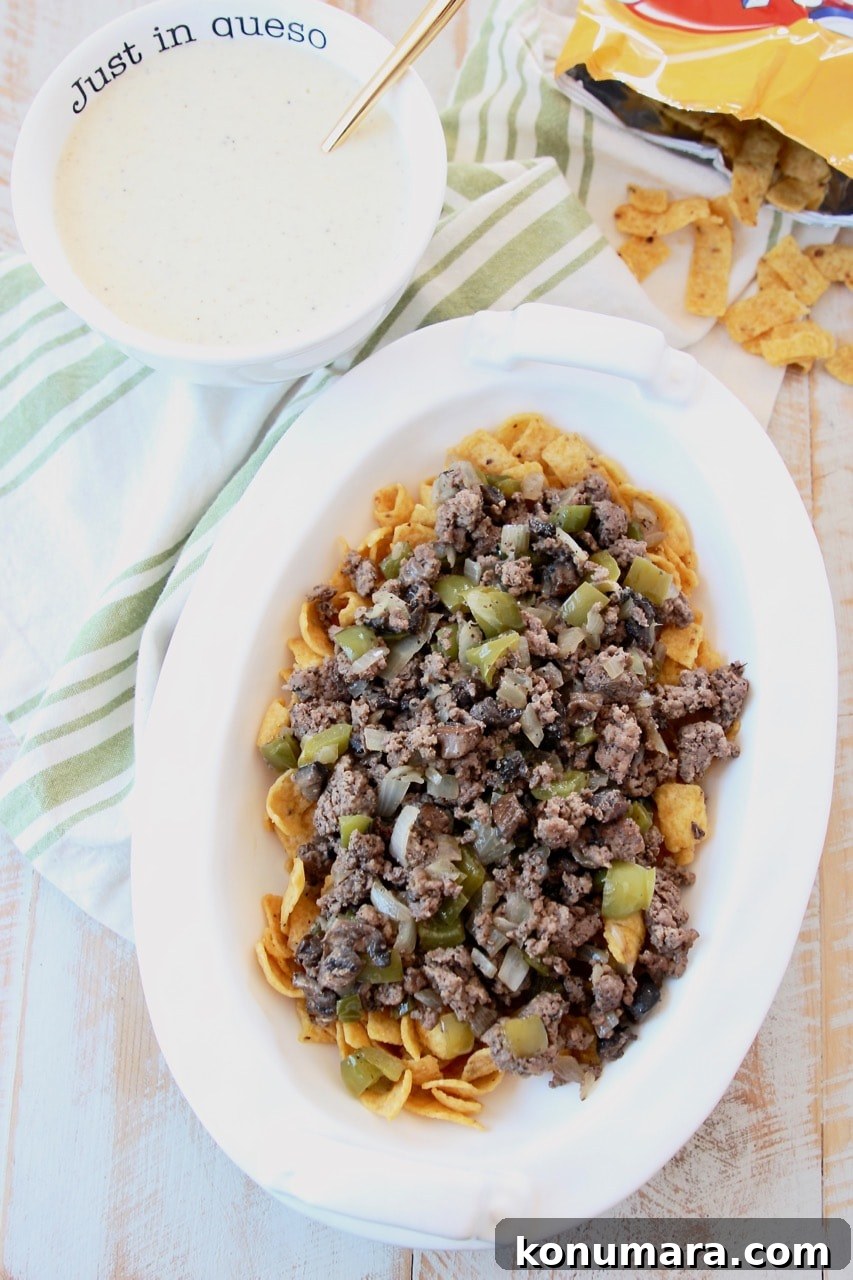 Frito pie topped with ground beef with a bowl of provolone cheese sauce and bag of fritos
