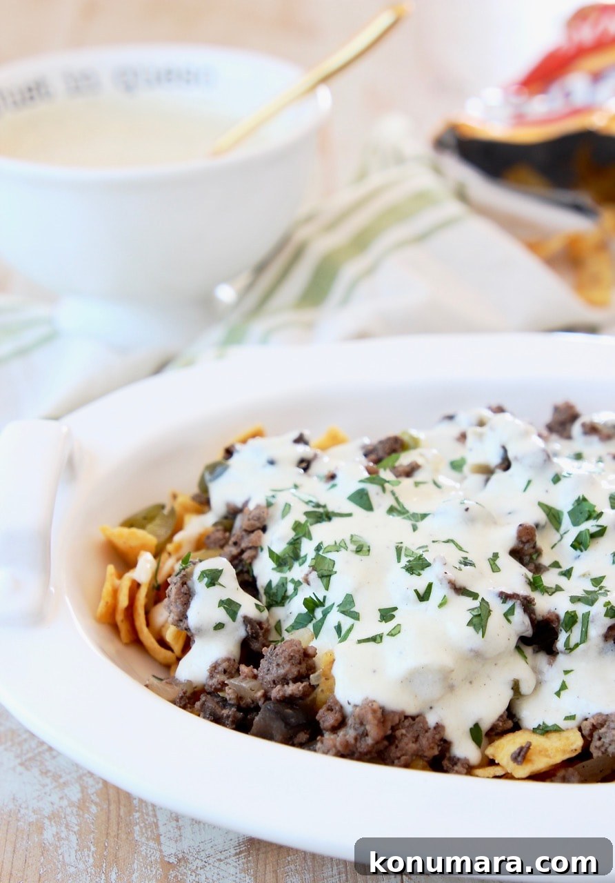 Philly Cheesesteak Frito Chili Pie in white casserole dish with Creamy Provolone Cheese Sauce and bag of Fritos