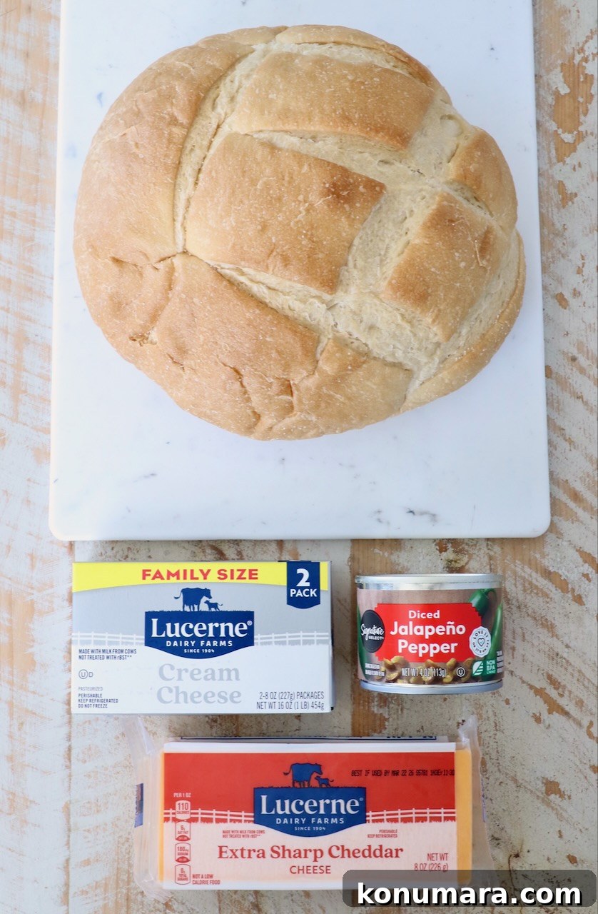 Cheesy Jalapeno Popper Bread Bowl Recipe 3 Round loaf of bread on a marble board, with cream cheese, extra sharp cheddar, and diced jalapeño peppers laid out on a rustic wooden table.