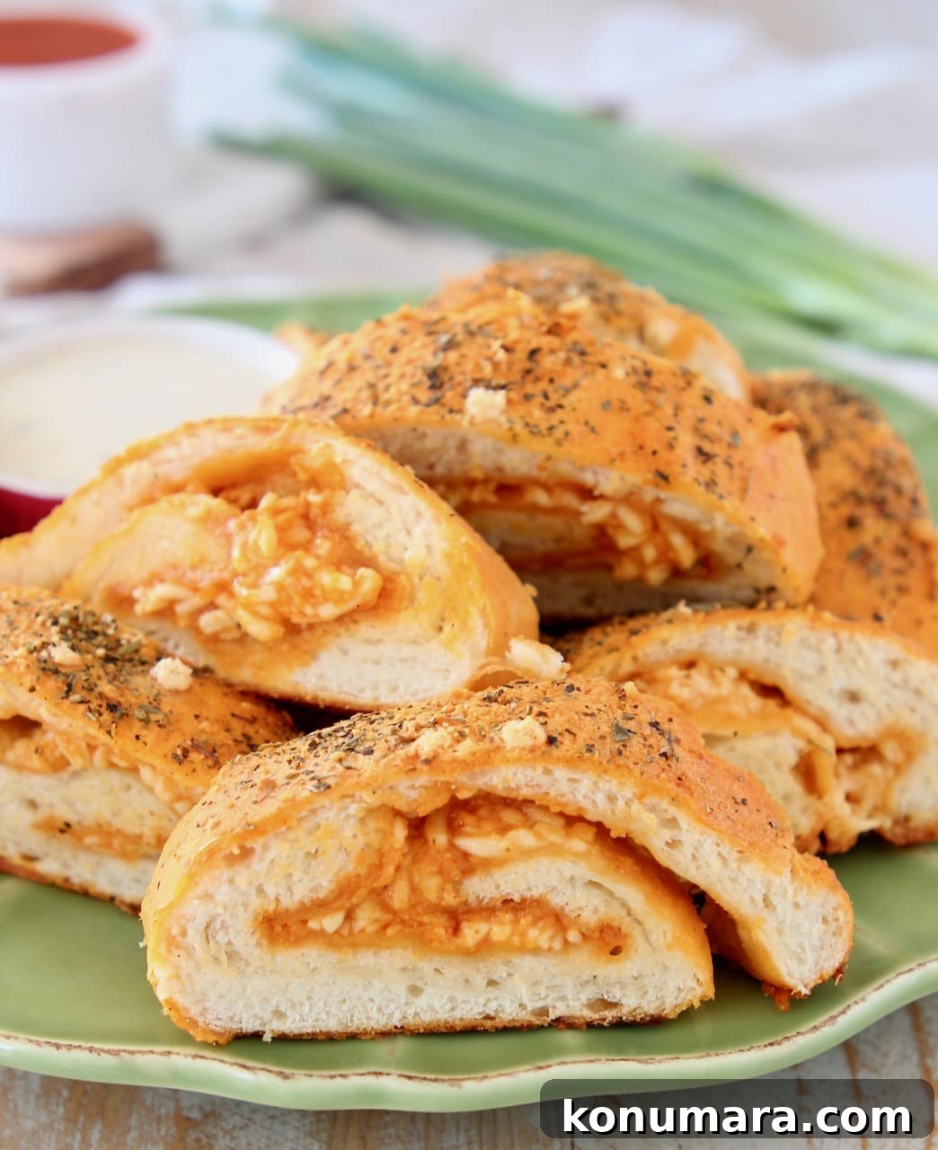 Cheesy Buffalo Chicken Pizza Bread 2 Pizza bread filled with buffalo garlic butter and cheese, sliced on green plate with small bowl of ranch dressing and green onions