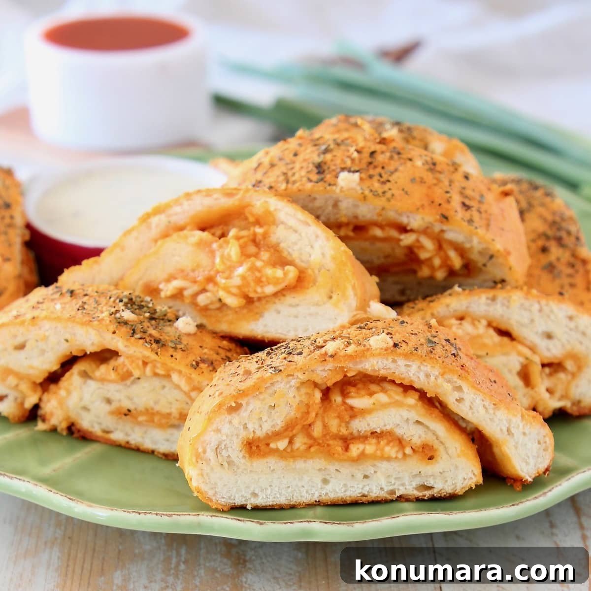 Cheesy Buffalo Chicken Pizza Bread 4 Pizza bread roll filled with buffalo sauce and cheese, sliced into pieces on a green plate with a ramekin of buffalo sauce and green onions