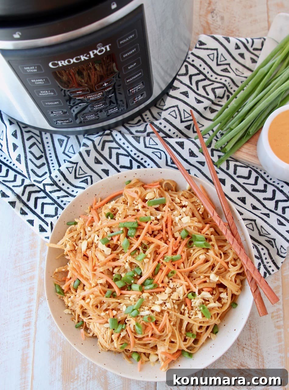 Pressure cooker chicken noodles with Thai peanut sauce in bowl with chopsticks, next to Crock Pot Express Crock machine