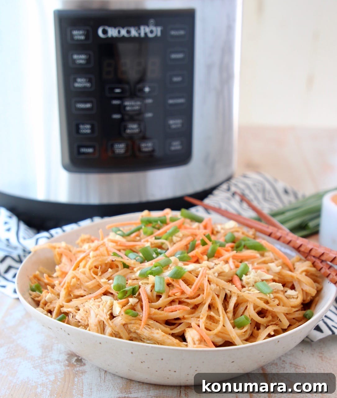 Crock Pot Express Crock Multi Cooker in background with bowl of Thai Peanut Chicken Noodles in front with chopsticks and green onions