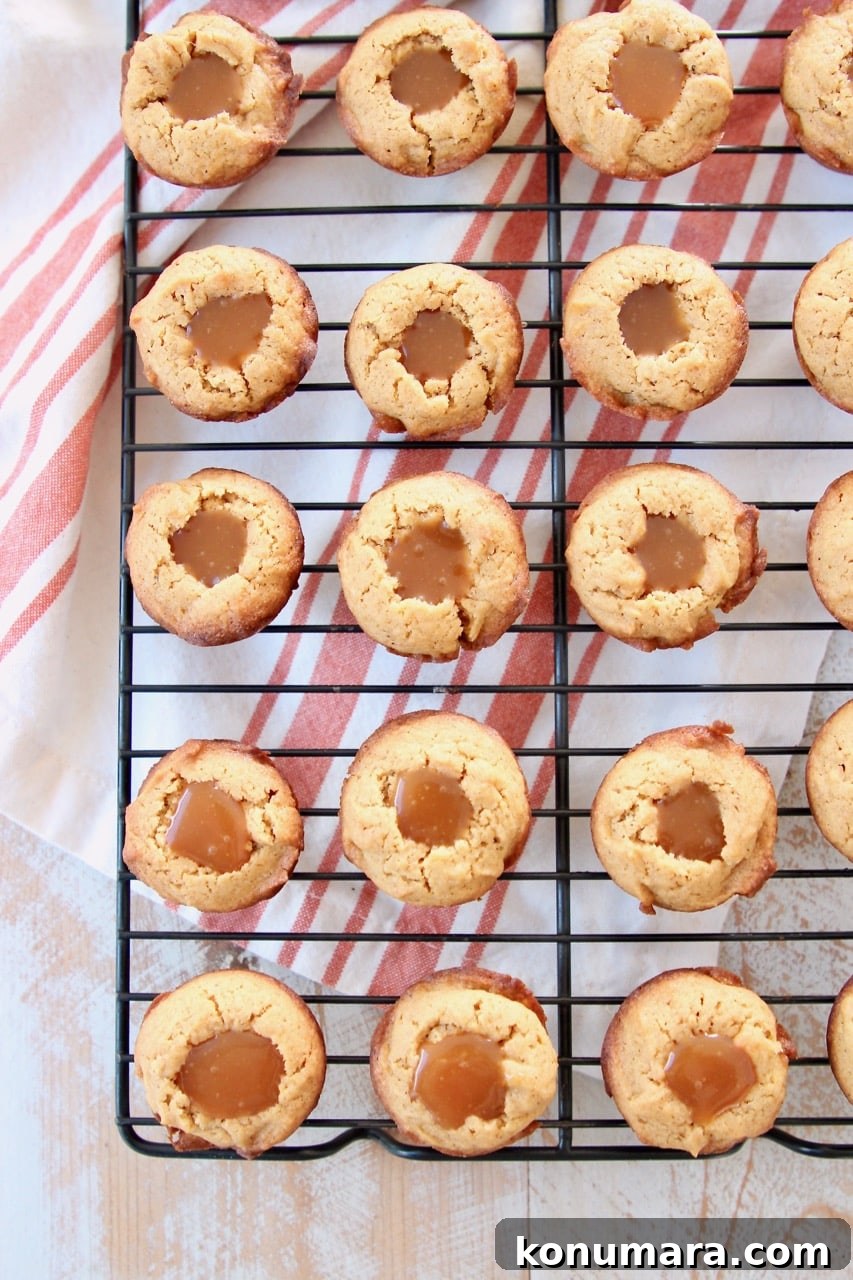 Salted Caramel Pumpkin Cookie Cups 7 Pumpkin cookie cups filled with salted caramel on black wire baking rack with orange striped towel