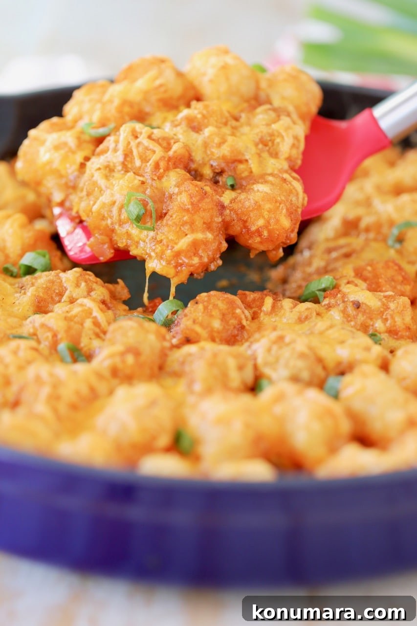 Buffalo Cheeseburger Tater Tot Casserole Recipe 2 Buffalo cheeseburger tater tot casserole in blue cast iron skillet with red spatula lifting casserole out of skillet