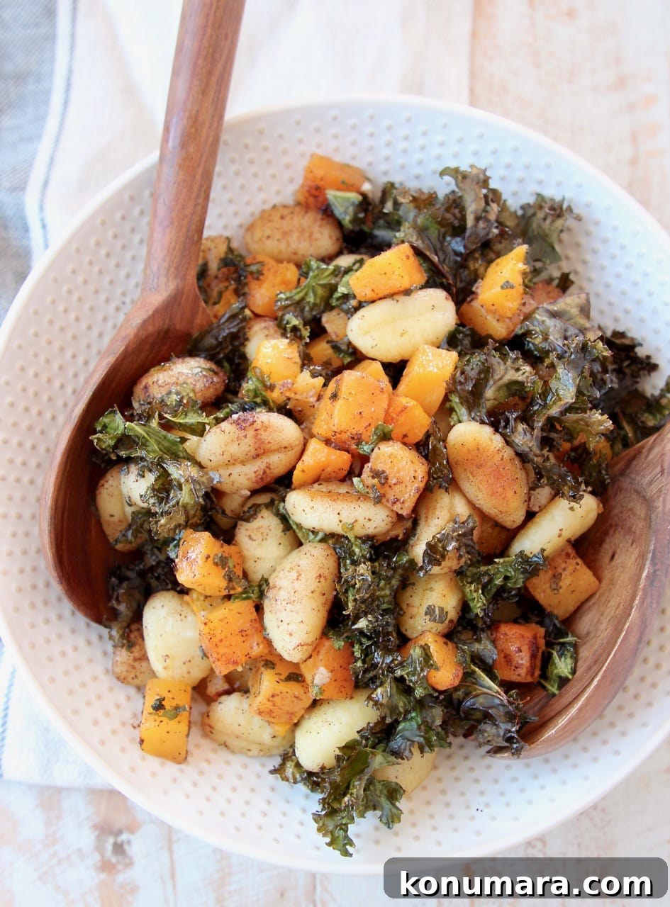 Gnocchi, butternut squash and kale in large white bowl with wooden serving spoons