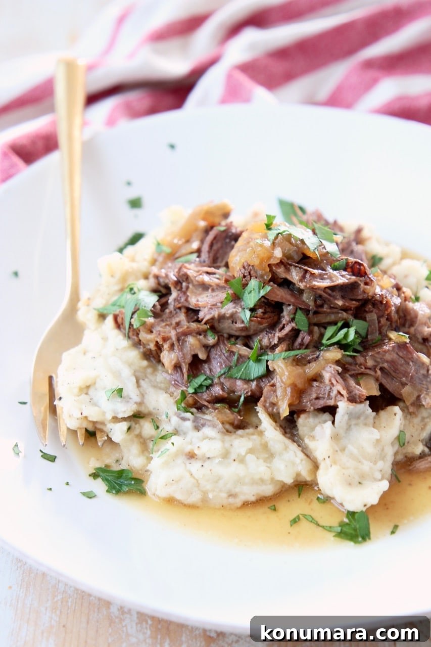 Savory French Onion Pot Roast with Caramelized Onions 2 Shredded pot roast with onions on top of mashed potatoes on white plate with gold fork and red and white striped towel