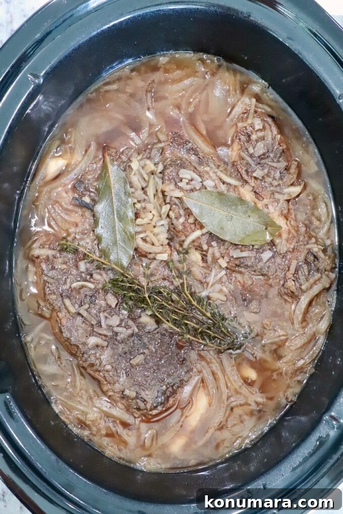 Savory French Onion Pot Roast with Caramelized Onions 11 cooked beef roast in a crock pot with beef stock, bay leaves and thyme sprigs