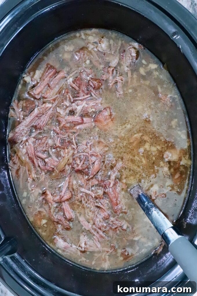 Savory French Onion Pot Roast with Caramelized Onions 12 shredded cooked pot roast in a crock pot in liquid with a serving spoon on the side