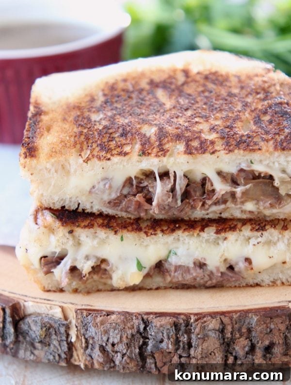 Savory French Onion Pot Roast with Caramelized Onions 14 Pot roast grilled cheese sandwich cut in half with melted gruyere cheese on wood cutting board with fresh parsley and small red ramekin of au jus