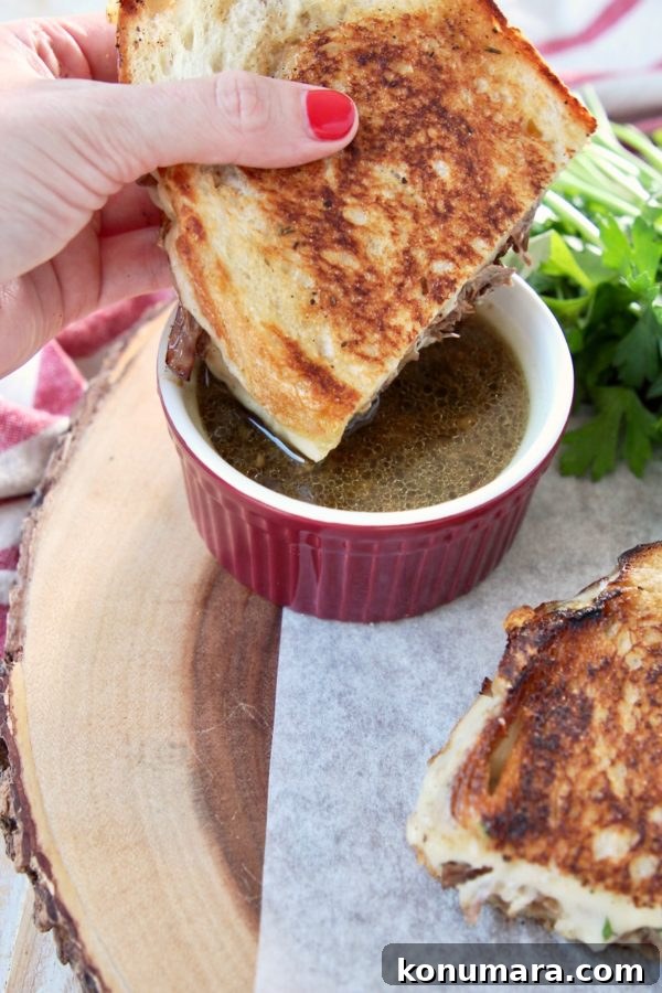 Savory French Onion Pot Roast with Caramelized Onions 15 Grilled cheese pot roast sandwich held in hand, being dipped into a red ramekin of au jus