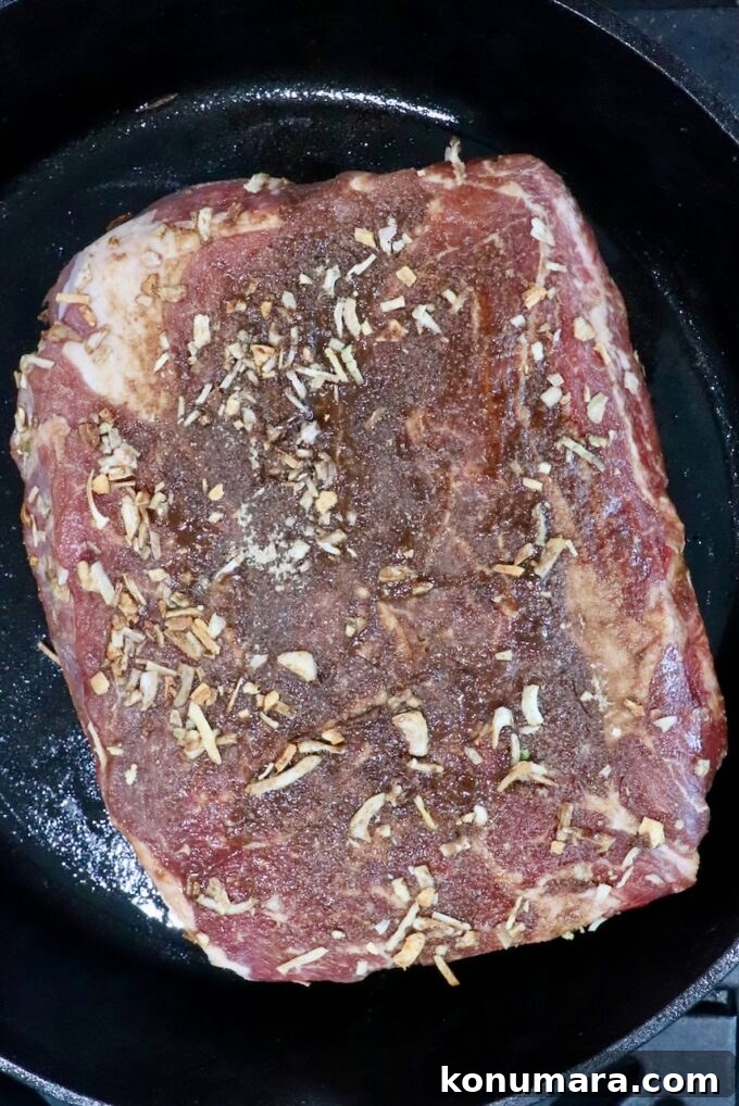 Savory French Onion Pot Roast with Caramelized Onions 7 seasoned raw beef roast in a cast iron skillet