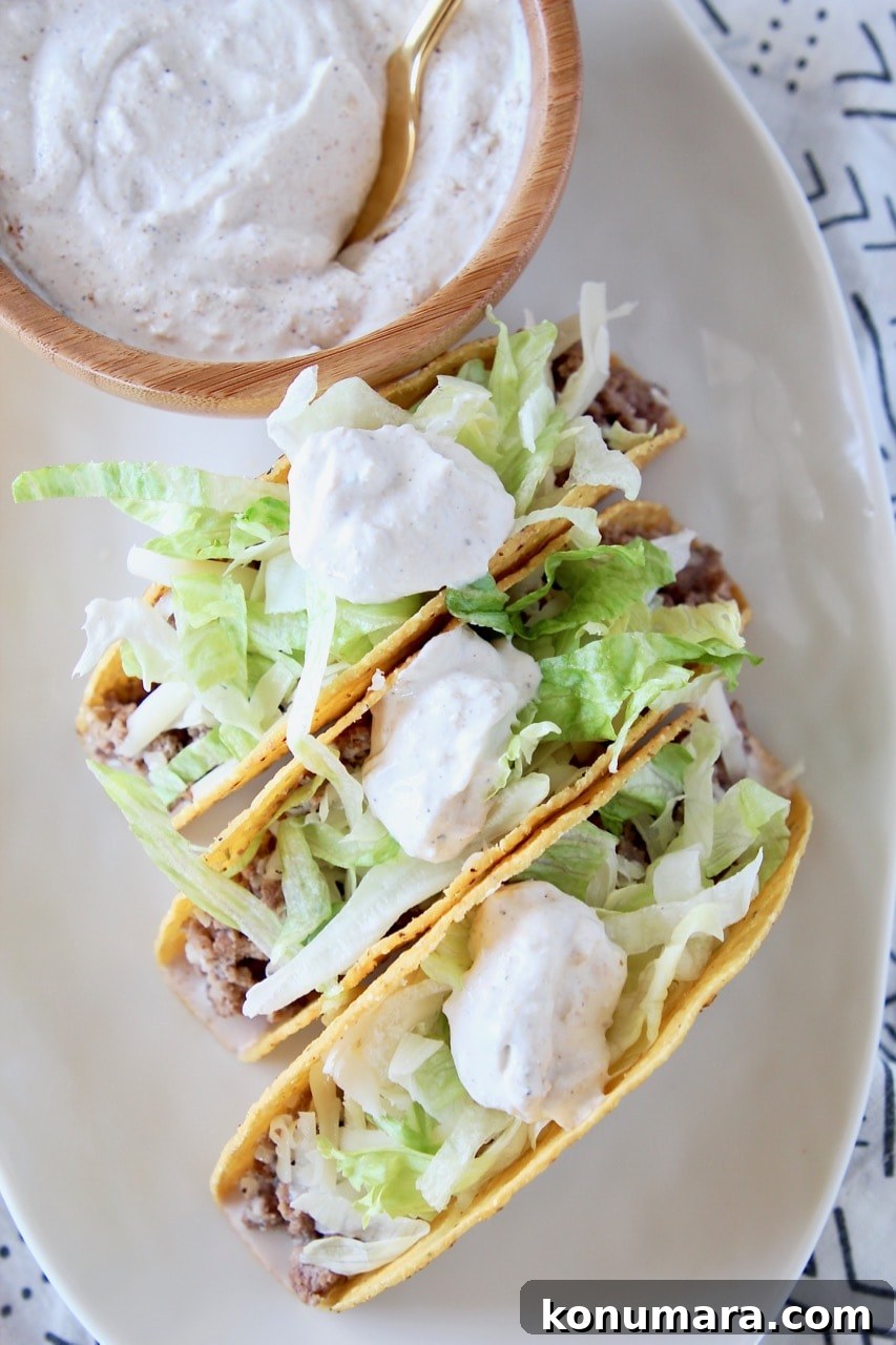 Ground beef tacos in crispy shells with shredded lettuce and french onion dip on plate with bowl of french onion dip