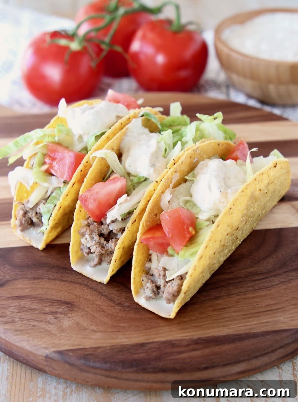 Ground beef tacos in crispy shells with french onion dip, diced tomatoes and shredded lettuce on wood cutting board with tomatoes on the vine and bowl of french onion dip