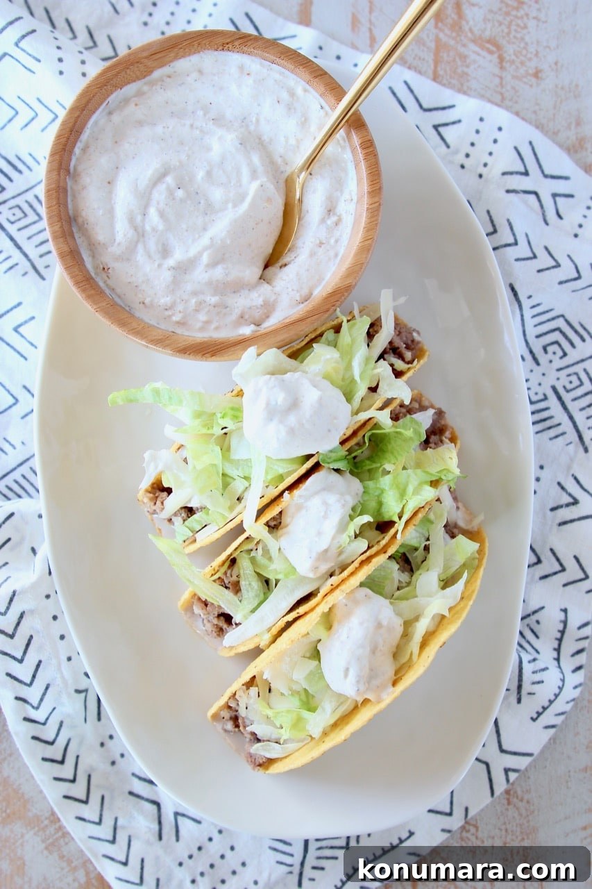 Ground beef tacos in crispy shell with shredded lettuce and french onion dip on plate with bowl of french onion dip with gold spoon