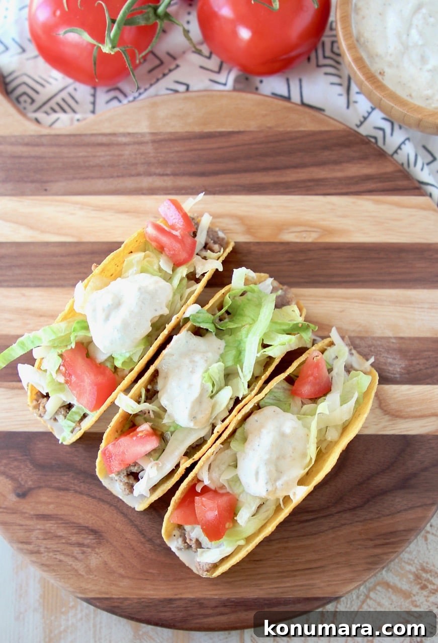 Crispy shell ground beef tacos on wood cutting board with tomatoes and french onion dip