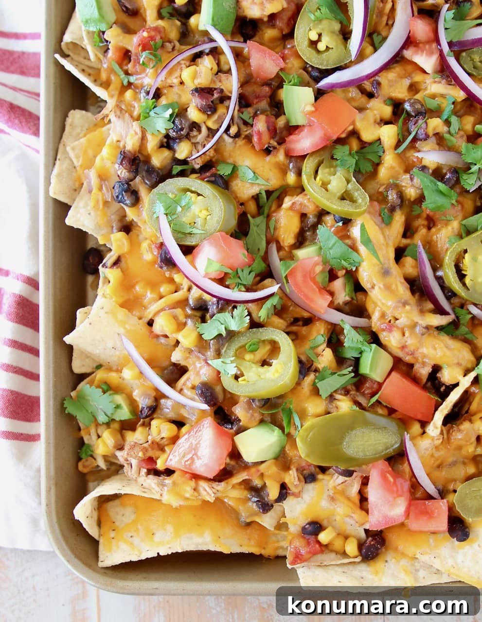 Cheesy Crock Pot Chicken Nachos Recipe 6 Chicken nachos on sheet pan with melted cheddar cheese, diced tomatoes, red onions and cilantro on red and white striped towel