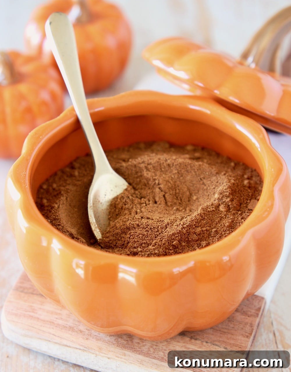 How to Make Pumpkin Pie Spice Blend 2 Homemade pumpkin pie spice in an orange pumpkin bowl with a small gold spoon and two small ceramic pumpkins