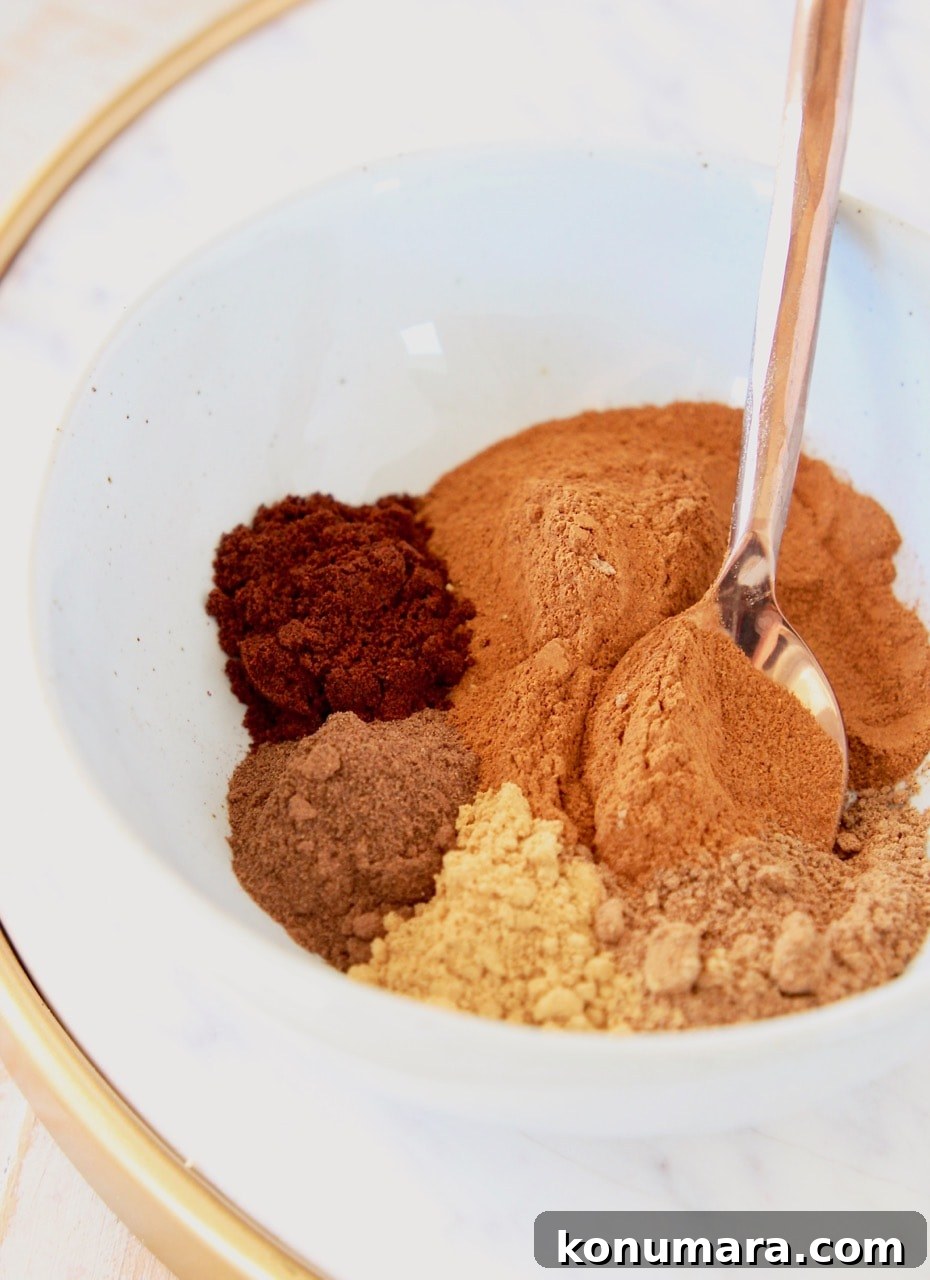 How to Make Pumpkin Pie Spice Blend 3 Ground cinnamon, nutmeg, ginger, cloves and allspice in white bowl with copper spoon on marble serving tray with gold handles