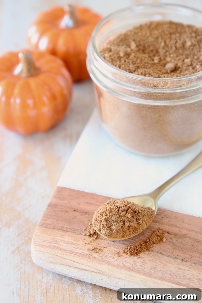 How to Make Pumpkin Pie Spice Blend 4 Small gold spoon with pumpkin pie spice on marble and wood cutting board with mason jar of pumpkin pie spice and two small orange ceramic pumpkins