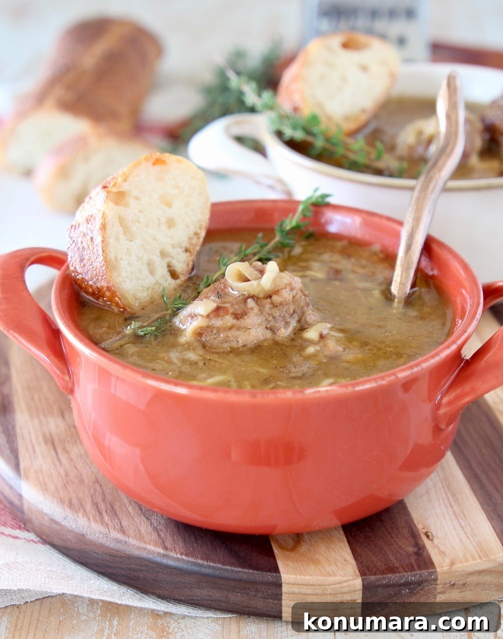 Slow Cooker French Onion Soup with Meatballs 3 French onion meatball soup in orange crock with fresh spring of thyme on top and copper spoon in the soup with a slice of bread on the side, sitting on a wood striped cutting board