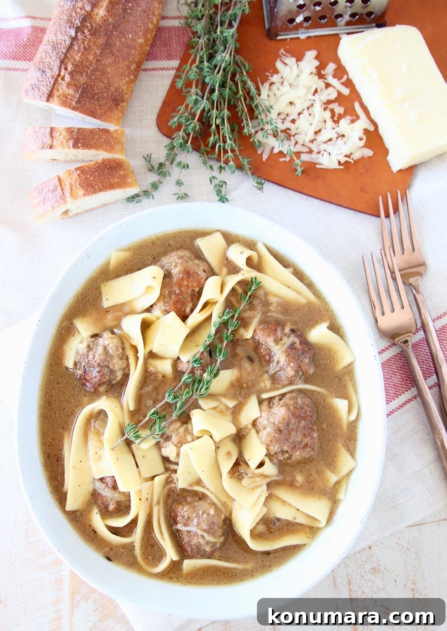 Slow Cooker French Onion Soup with Meatballs 6 Bowl of egg noodles, meatballs and thyme sprigs on red striped towel with two copper forks and sliced baguette on cutting board
