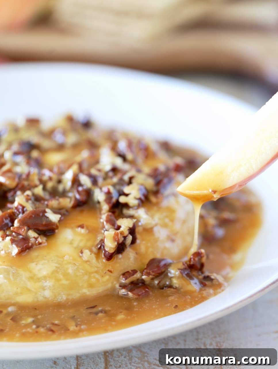 Salted Caramel Pecan Baked Brie Recipe 6 Apple slice dipped into salted caramel poured over baked brie with pecans on white plate