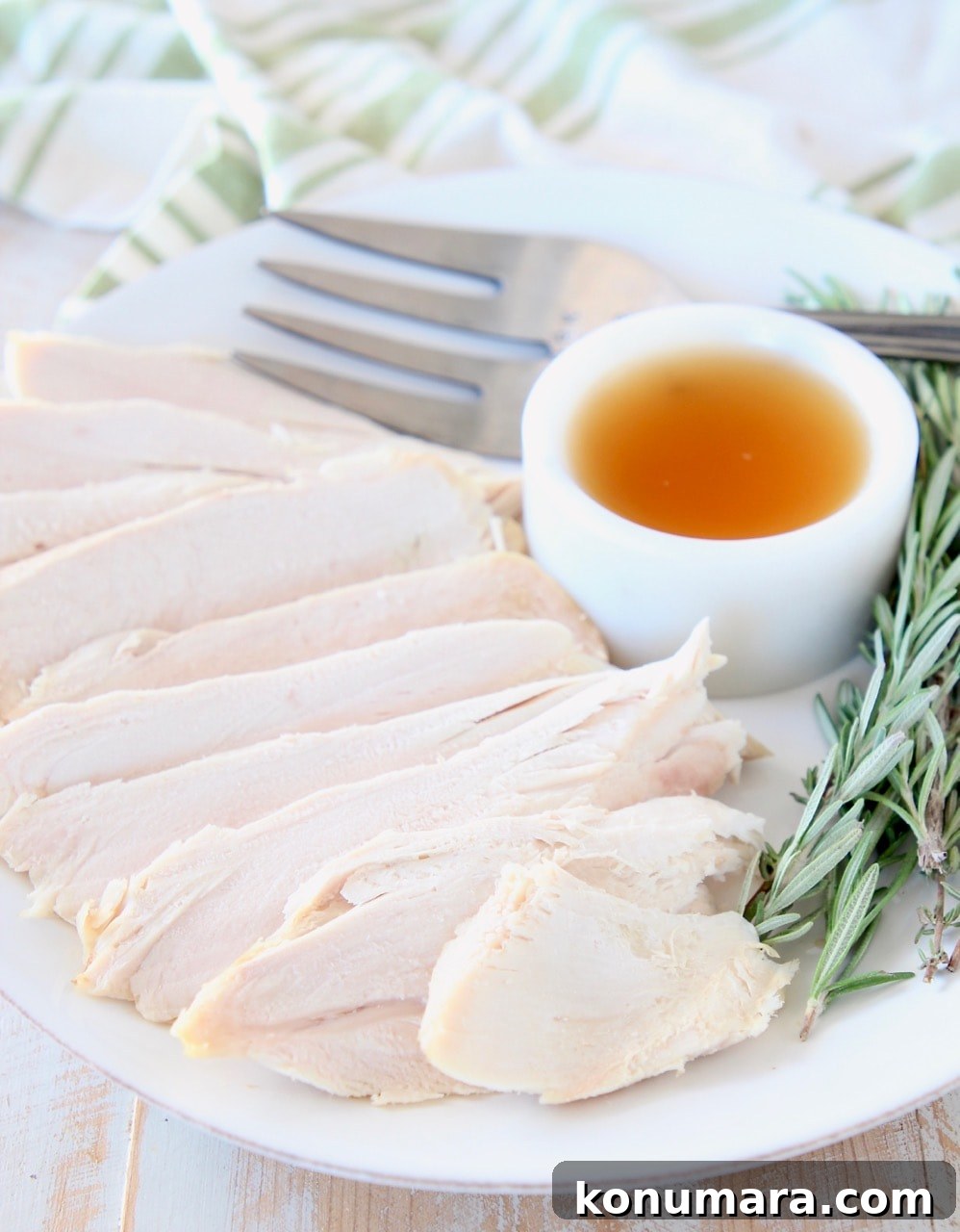 Sliced turkey on white plate with ramekin of maple apple reduction and rosemary sprigs