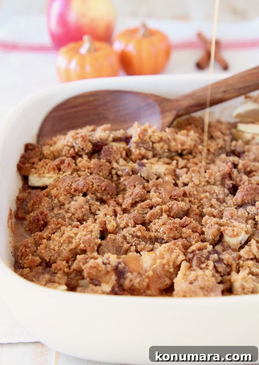 Pumpkin spice apple crumble in casserole dish with wooden spoon and drizzle of caramel syrup, with small ceramic pumpkins in background