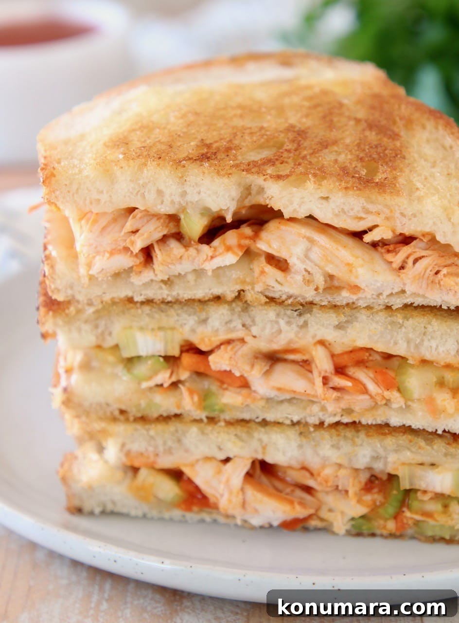 Crispy Buffalo Turkey Grilled Cheese Recipe 2 Buffalo turkey grilled cheese sandwiches, sliced in half diagonally, stacked up on white plate with fresh parsley in the background