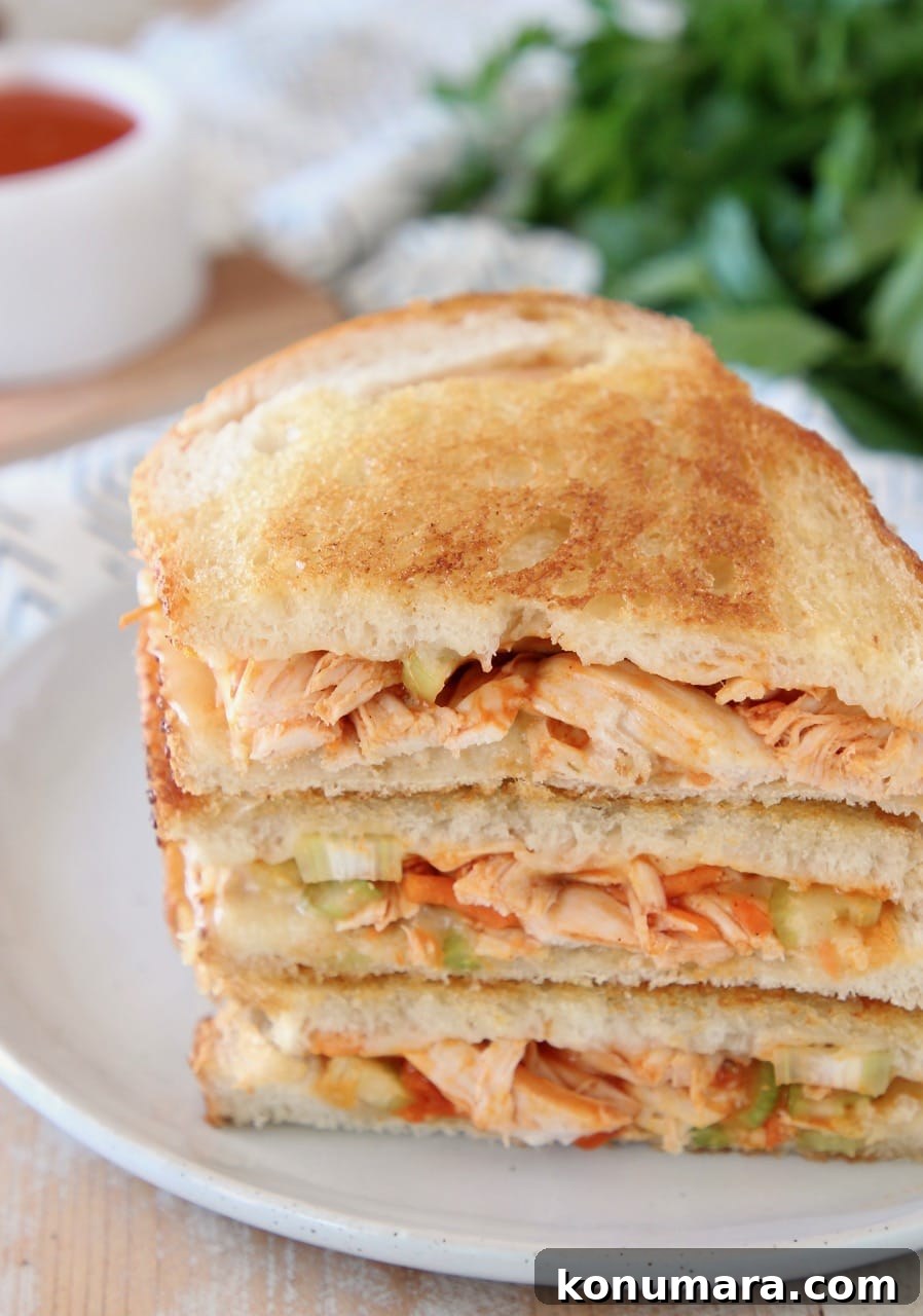 Crispy Buffalo Turkey Grilled Cheese Recipe 3 Buffalo turkey grilled cheese sandwiches, sliced in half diagonally, stacked up on white plate with fresh parsley in the background