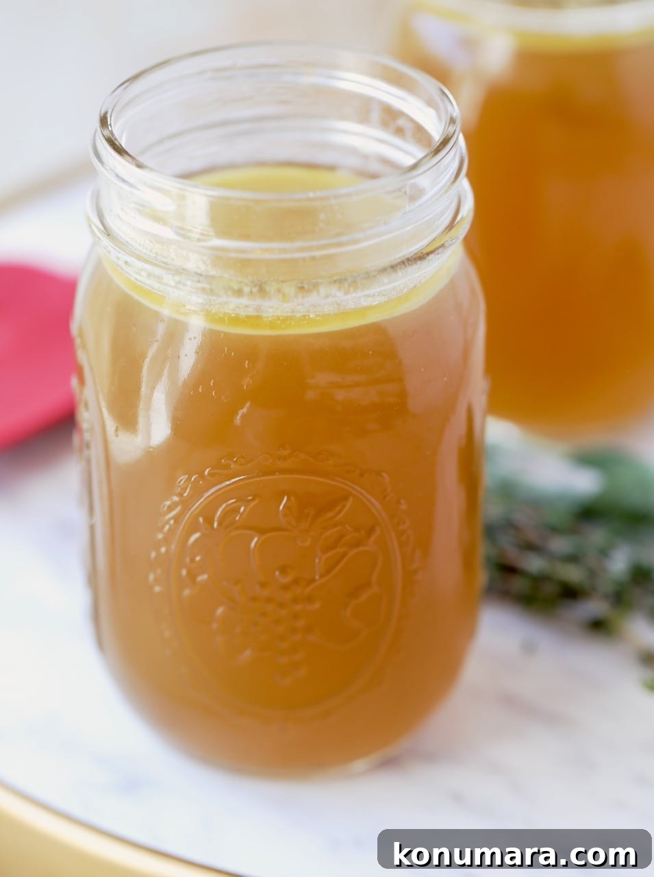 Mason jar of homemade instant pot turkey stock on marble tray with sprigs of fresh thyme and sage