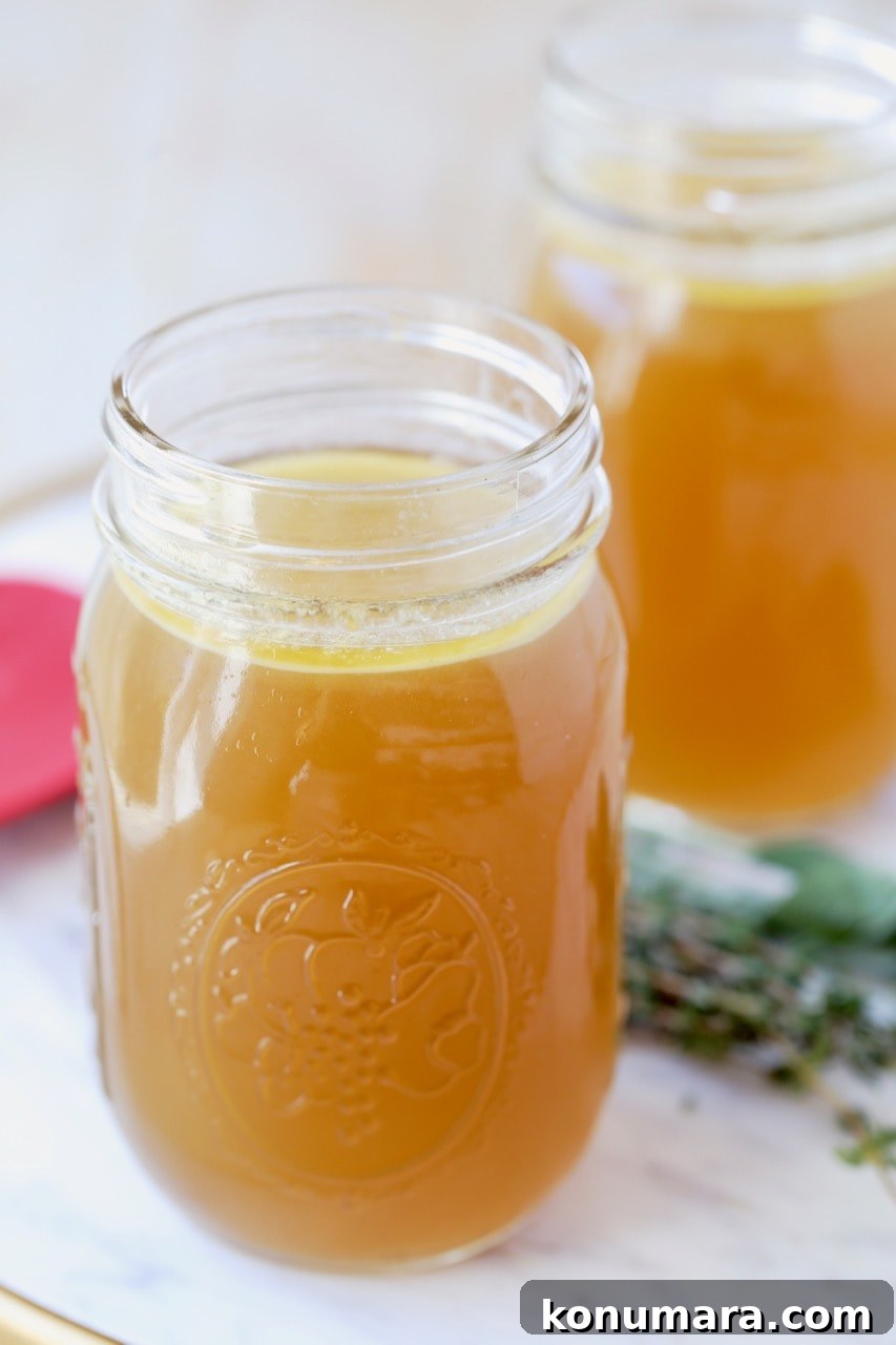 Instant pot turkey stock in 16 oz mason jars on marble tray with red spatula and fresh thyme and sage leaves