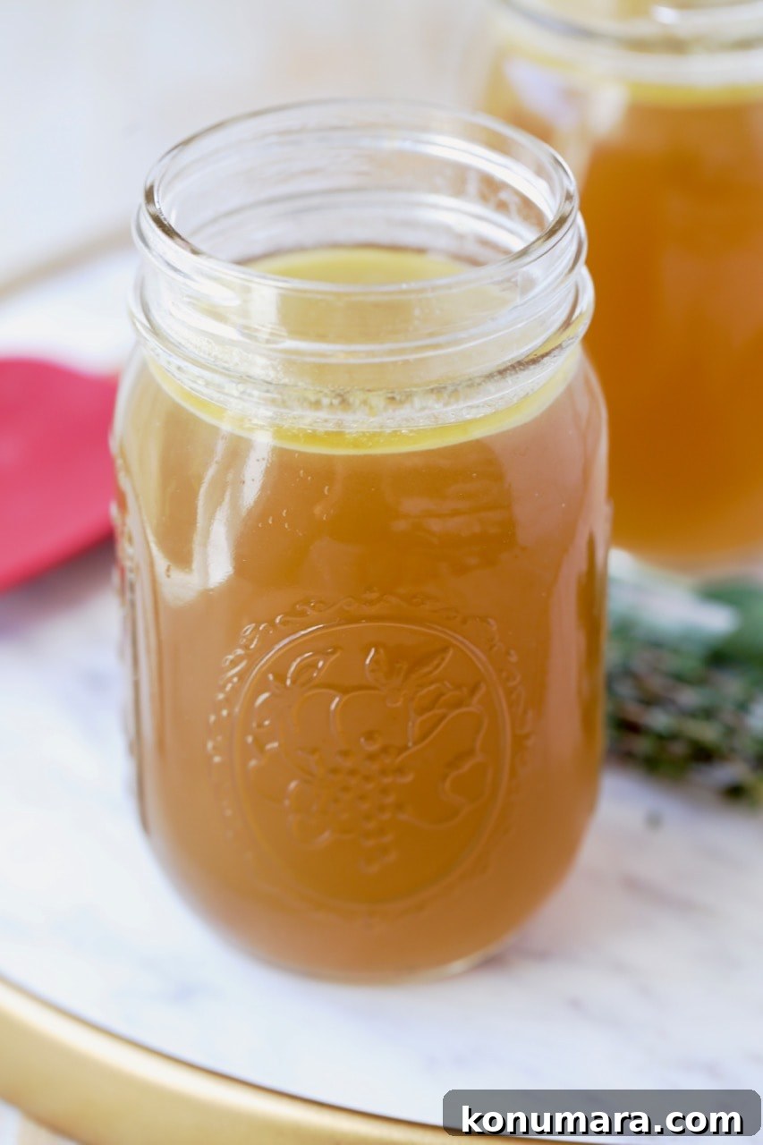 Instant pot turkey stock in mason jar on marble tray with fresh herbs and red spatula