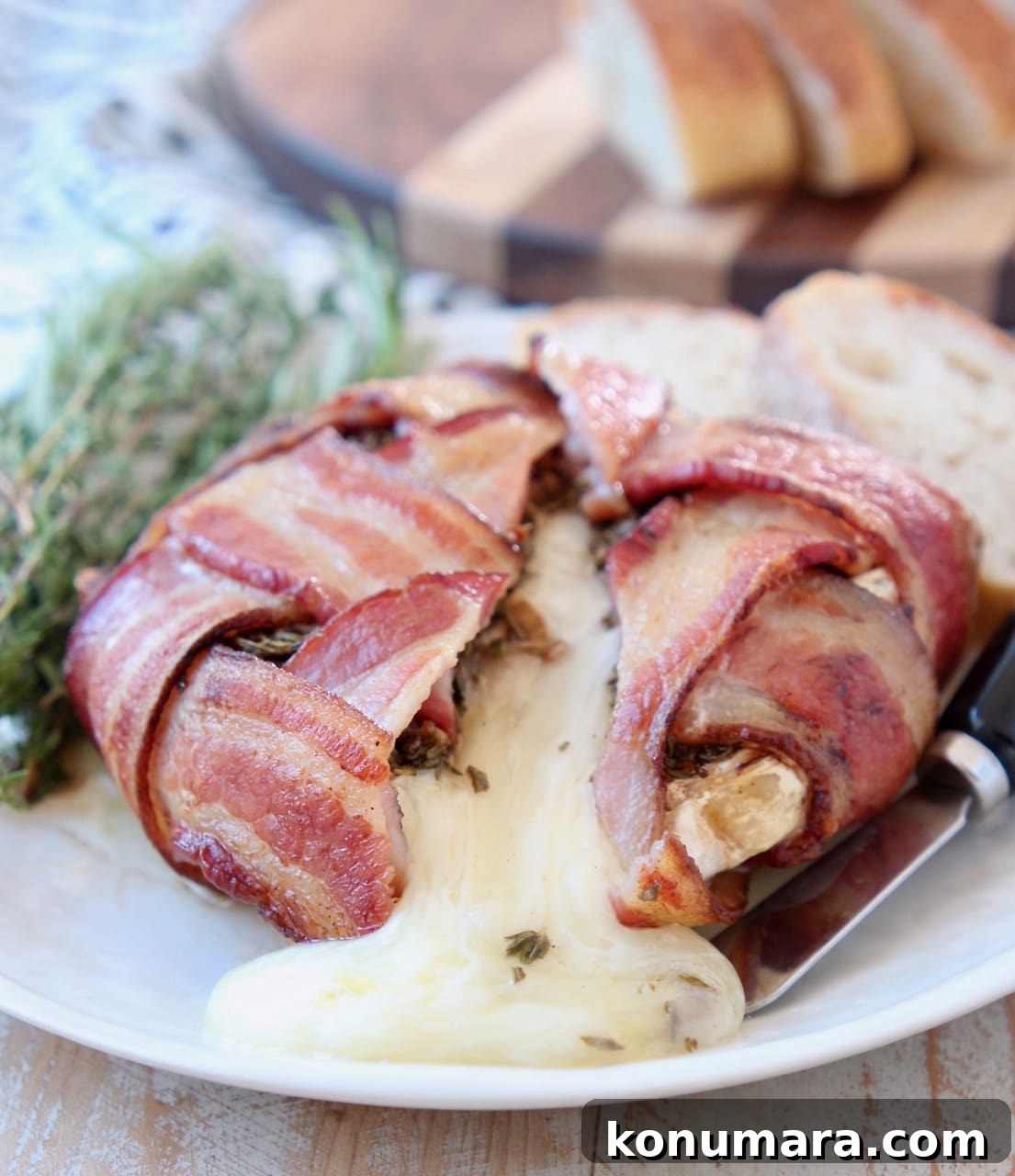 Garlic Herb Bacon-Wrapped Brie Bites 2 Baked brie cheese melted out of bacon wrapped brie with fresh herbs on plate and sliced baguette, with black cheese spreader