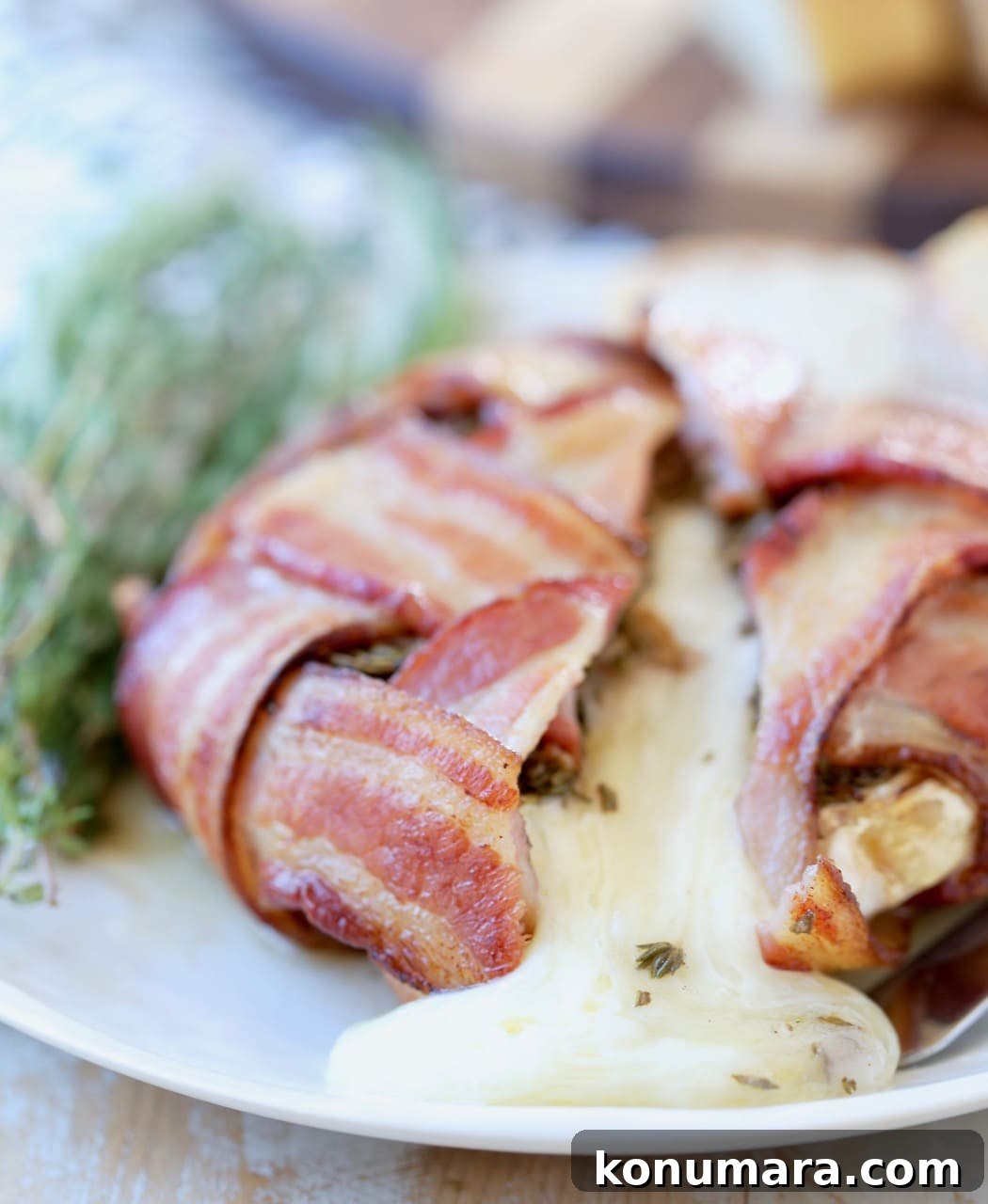 Garlic Herb Bacon-Wrapped Brie Bites 5 Bacon Wrapped Brie with melty brie cheese spilling out onto white plate with fresh herbs on the side and a sliced baguette behind it