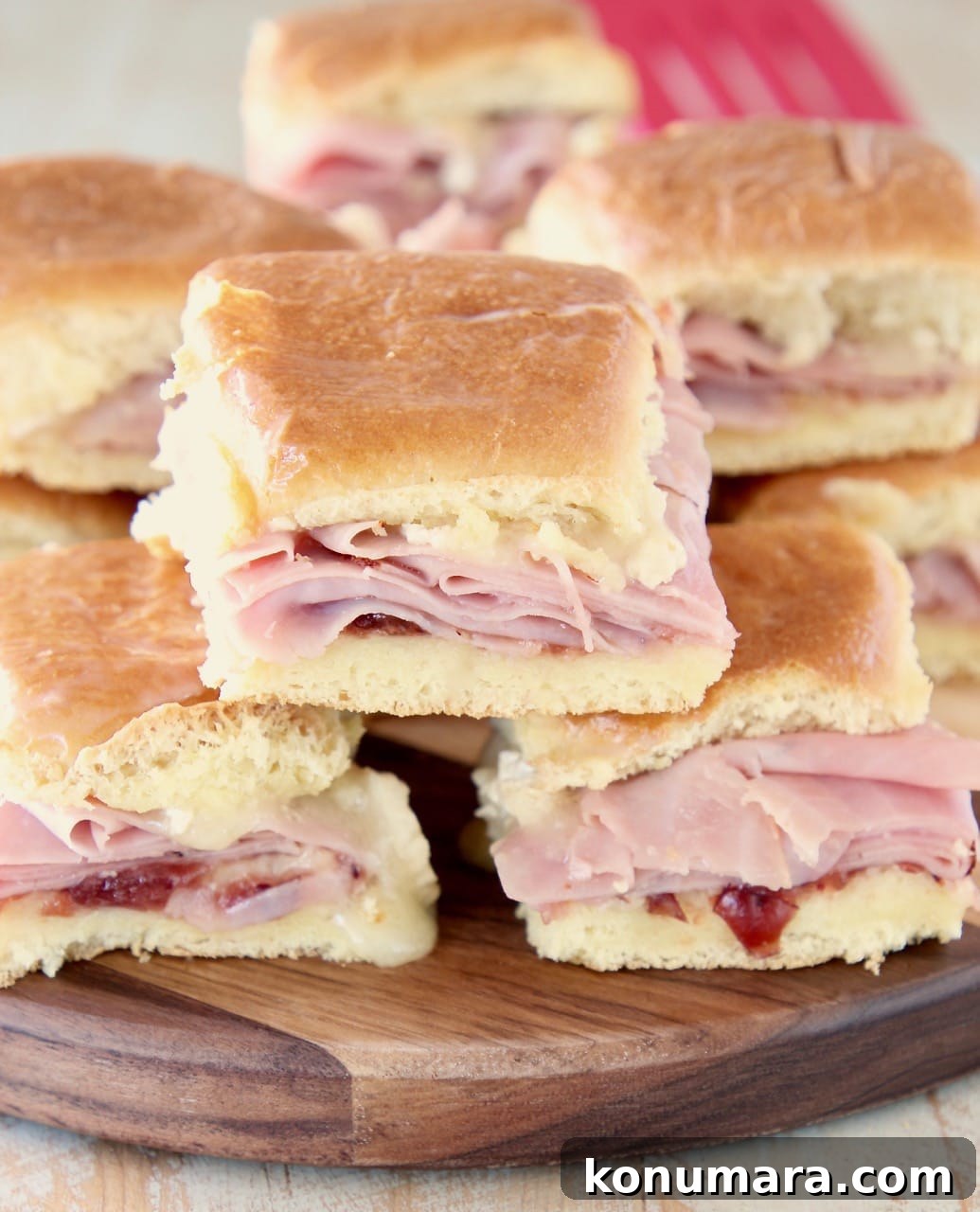 Cranberry, Brie and Ham Sliders Recipe 3 Ham sliders on Hawaiian Rolls stacked on each other on a wood cutting board