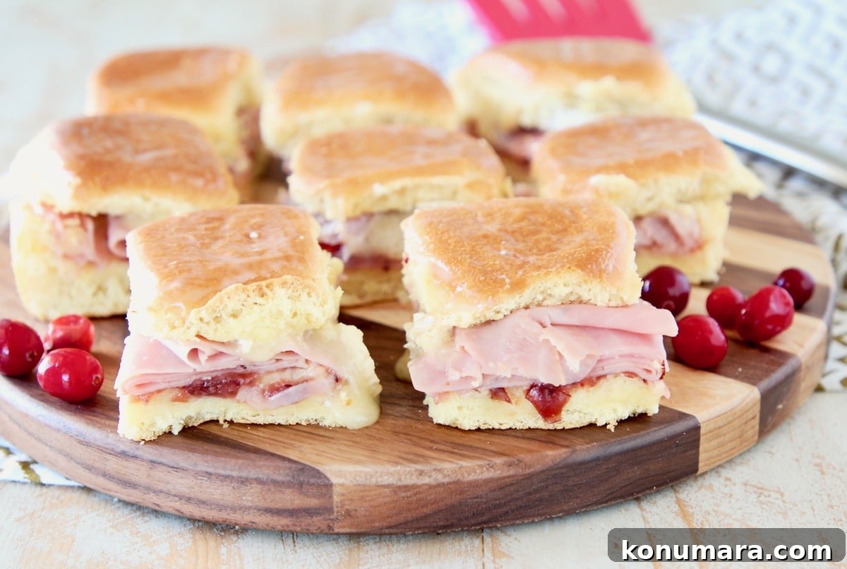 Cranberry, Brie and Ham Sliders Recipe 4 Ham sliders with cranberry sauce and brie cheese on hawaiian rolls, sitting on a wood cutting board with red spatula in background