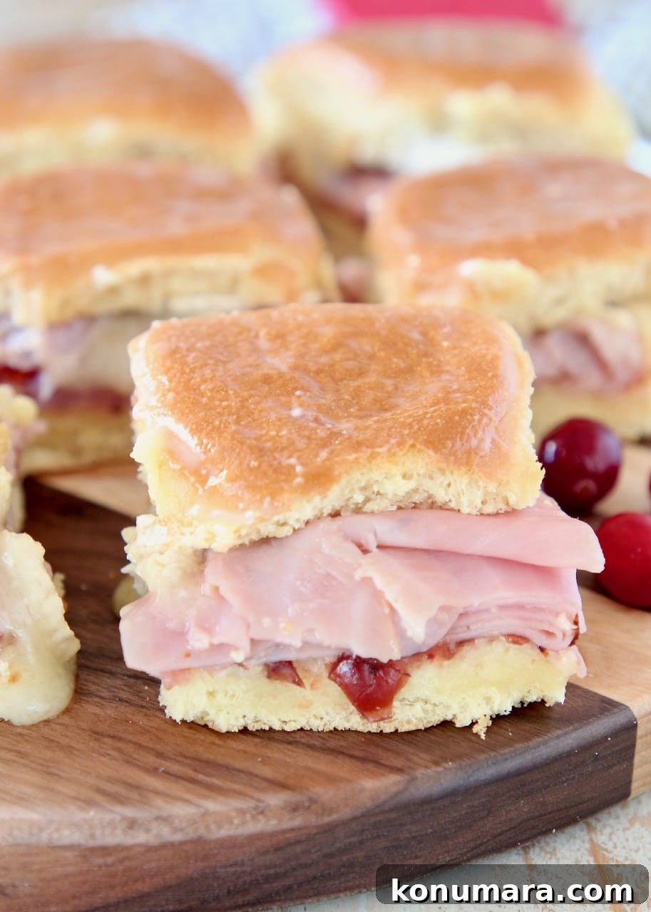Cranberry, Brie and Ham Sliders Recipe 5 Ham Sliders on Hawaiian rolls with cranberry sauce, sitting on wood cutting board with fresh cranberries