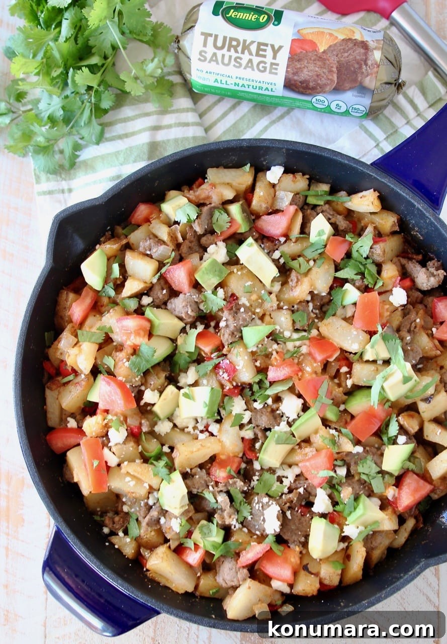 Breakfast hash in blue cast iron skillet, filled with diced potatoes, turkey sausage, avocado, tomatoes and queso fresco, with fresh cilantro and a package of Jennie-O turkey sausage