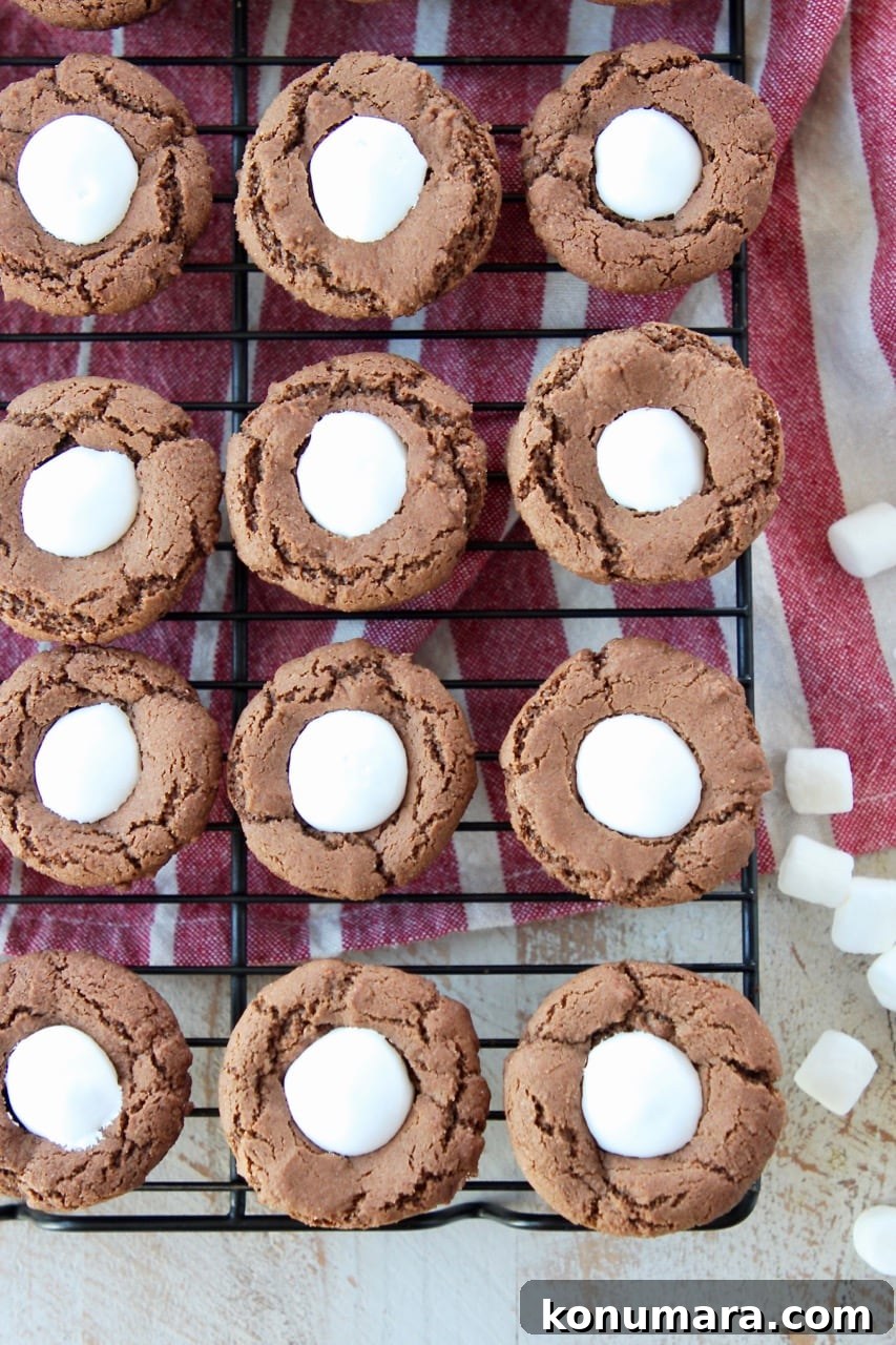 Overhead shot of chocolate cookie cups filled with marshmallow creme on top of red and white striped towel with mini marshmallows on the side