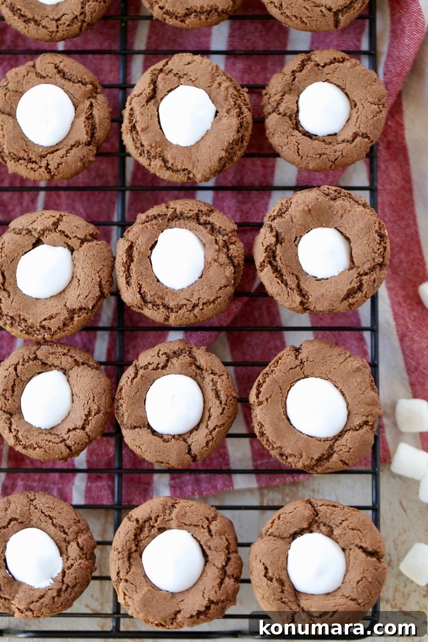 Hot chocolate cookie cups filled with marshmallow creme on black wire rack with a red and white striped towel underneath