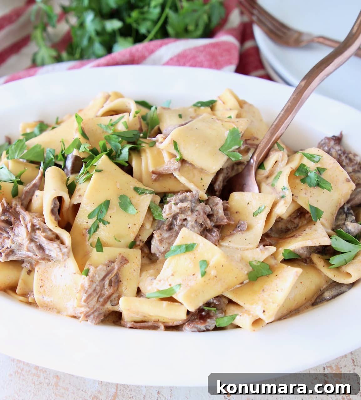 Creamy Instant Pot Beef Stroganoff 5 Instant pot beef stroganoff with wide egg noodles and fresh parsley in white serving bowl, with copper fork in bowl