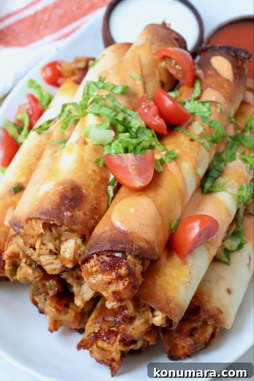 air fried chicken taquitos stacked up on a plate topped with chopped lettuce and tomatoes