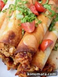 buffalo chicken taquitos stacked up on a plate topped with shredded lettuce and diced tomatoes