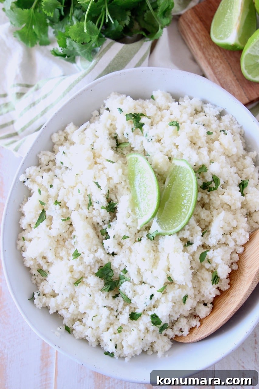 Zesty Cilantro Lime Cauliflower Rice Recipe 2 Large white bowl of cilantro lime cauliflower rice with two lime wedges on top and wooden spoon in the bowl