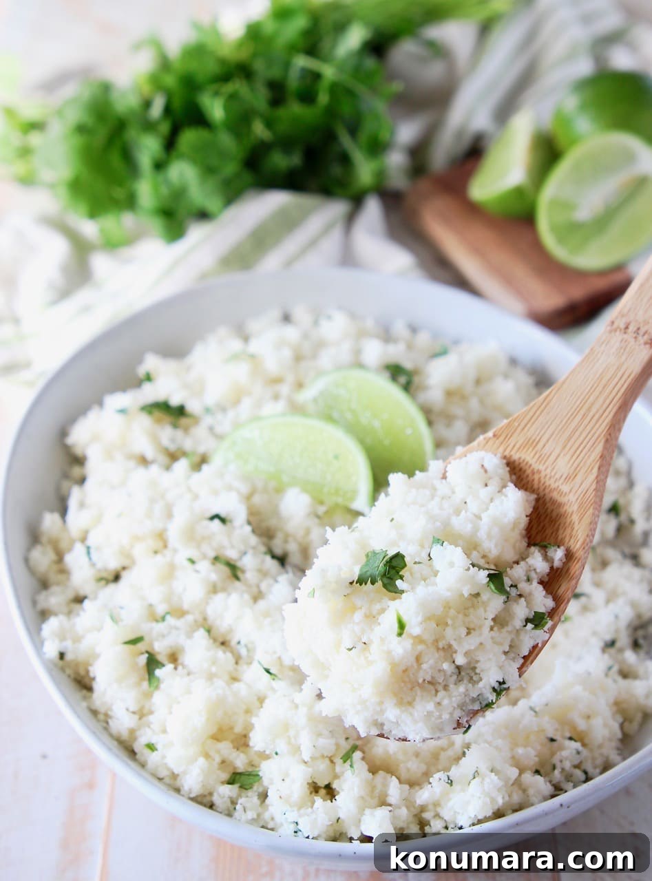 Zesty Cilantro Lime Cauliflower Rice Recipe 3 Wooden spoon of cilantro lime cauliflower rice coming out of a bowl of cauliflower rice with lime wedges on top and fresh cilantro in the background