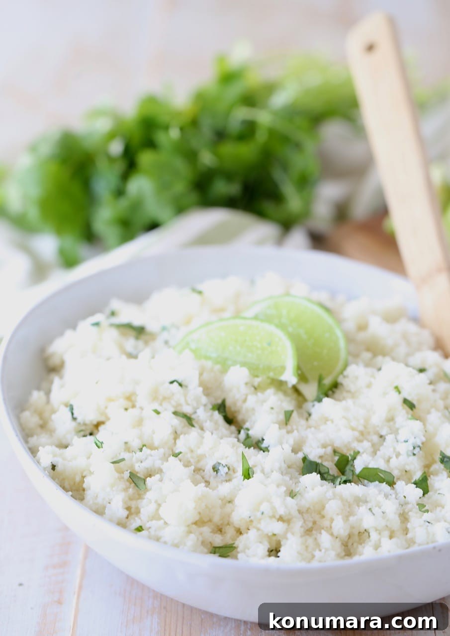 Zesty Cilantro Lime Cauliflower Rice Recipe 4 Cilantro lime cauliflower rice in white bowl with lime wedges on top and wooden spoon in bowl, with fresh cilantro in background