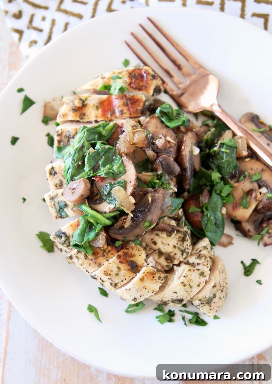 Sliced grilled chicken breast on white plate, topped with mushrooms and spinach, with copper fork on side of plate