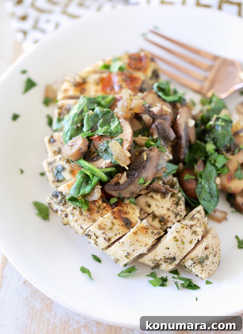 Grilled sliced chicken on plate, topped with sauteed mushrooms and spinach with copper fork on side of plate, garnished with fresh chopped parsley